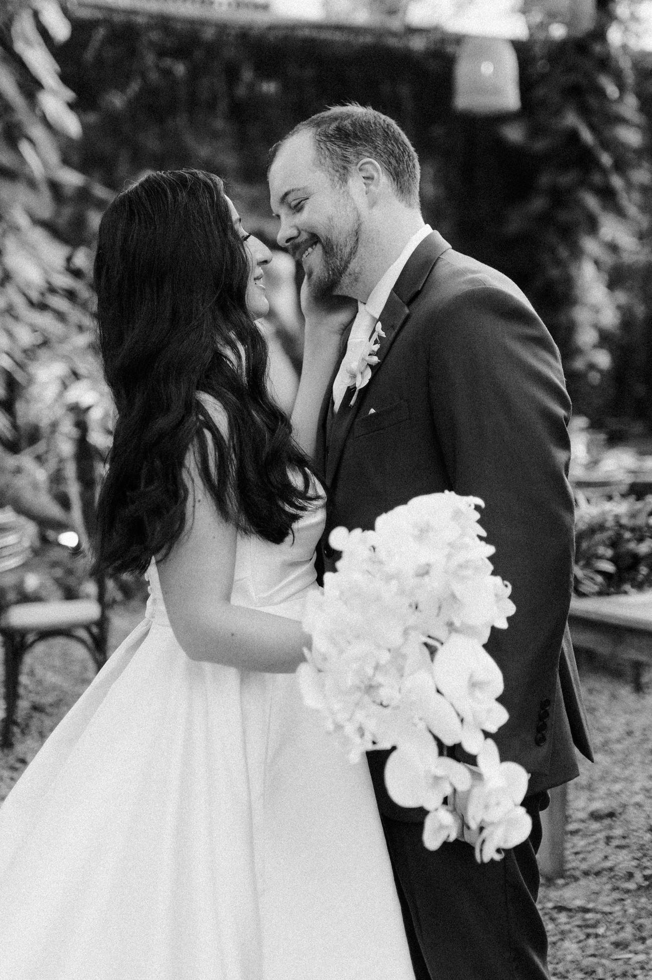 Destination wedding photographer — black and white portrait of a couple sharing a kiss with an orchid bouquet