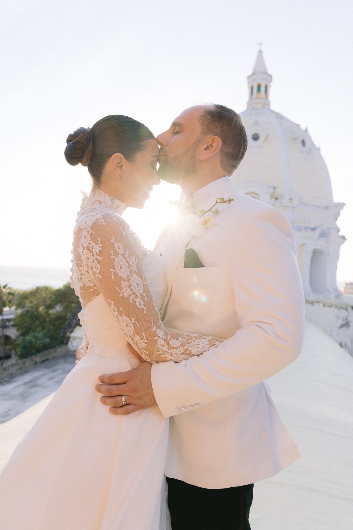 Couple sharing a forehead kiss with dramatic sun flare after a proposal in Cartagena