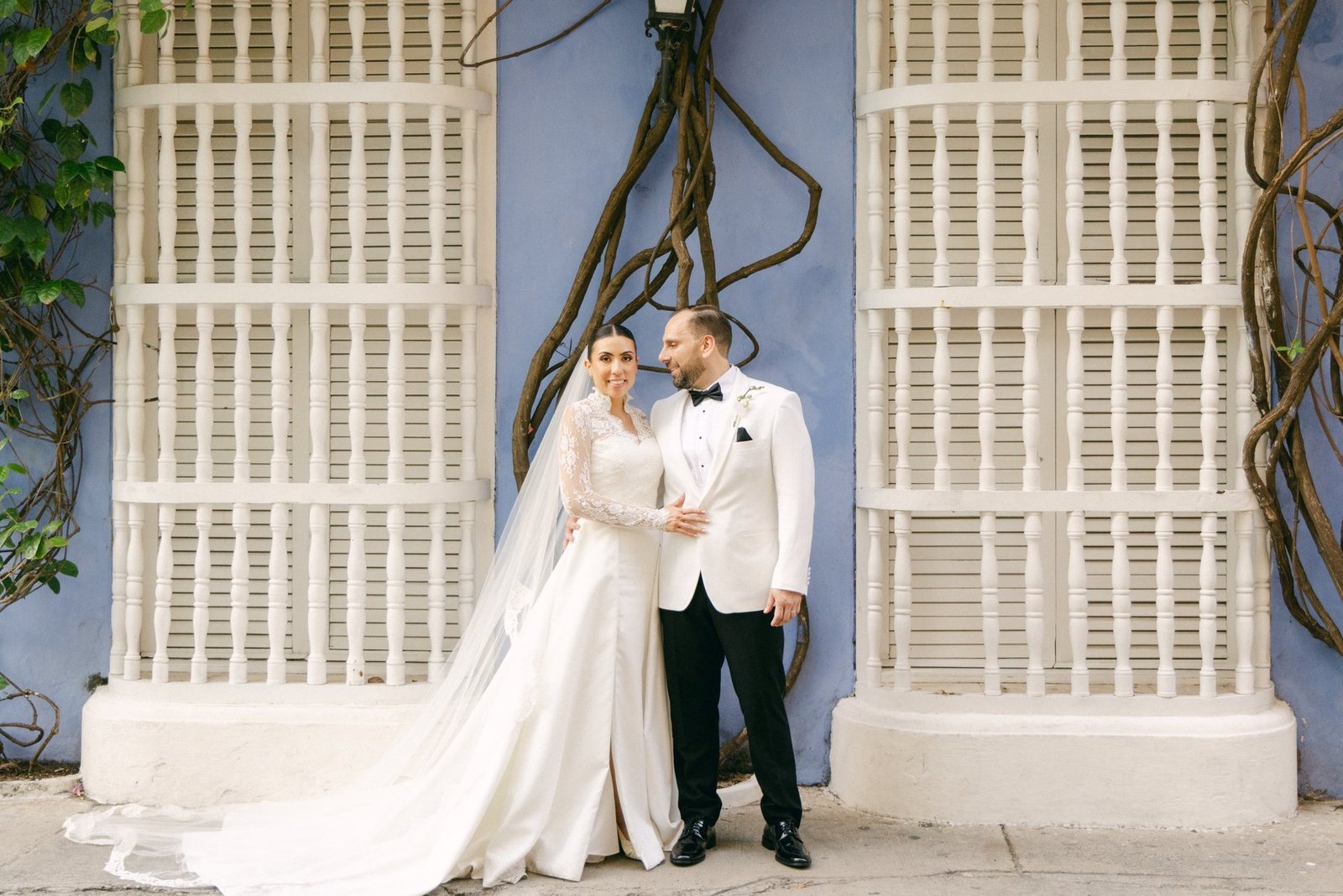 Editorial couple portrait against a vine-covered blue wall