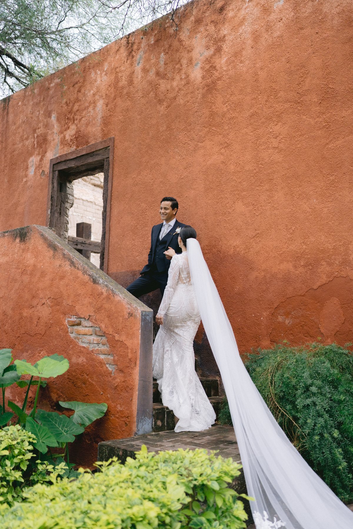 Bride's veil trailing down a colonial staircase against a terracotta wall